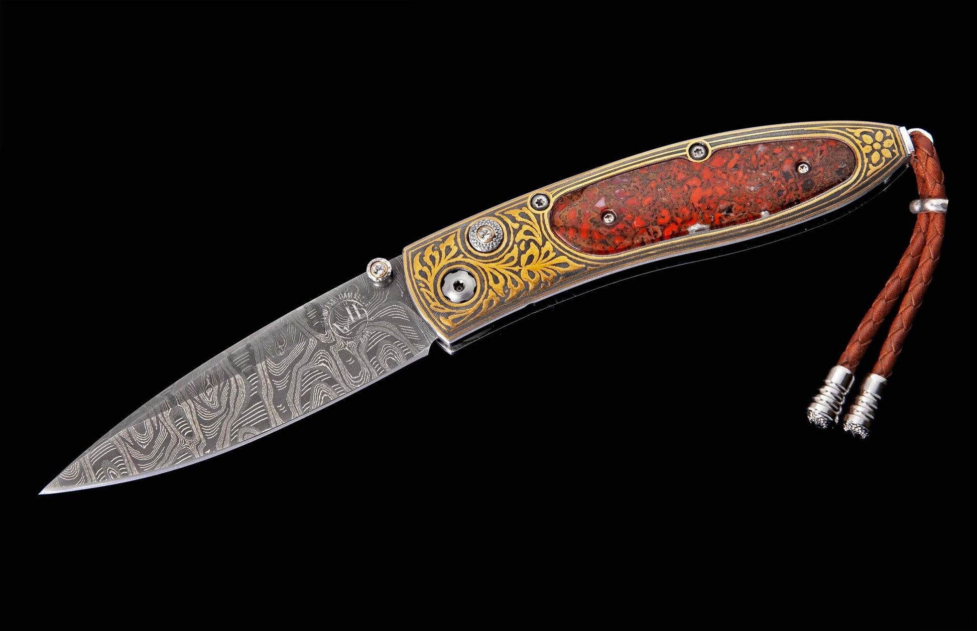 Ornate folding knife with a Damascus steel blade, engraved gold handle, a red stone insert, and a braided leather lanyard.