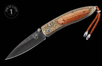 Ornate folding knife with dark damascus blade, gold engraved details, burl wood handle, and leather lanyard.