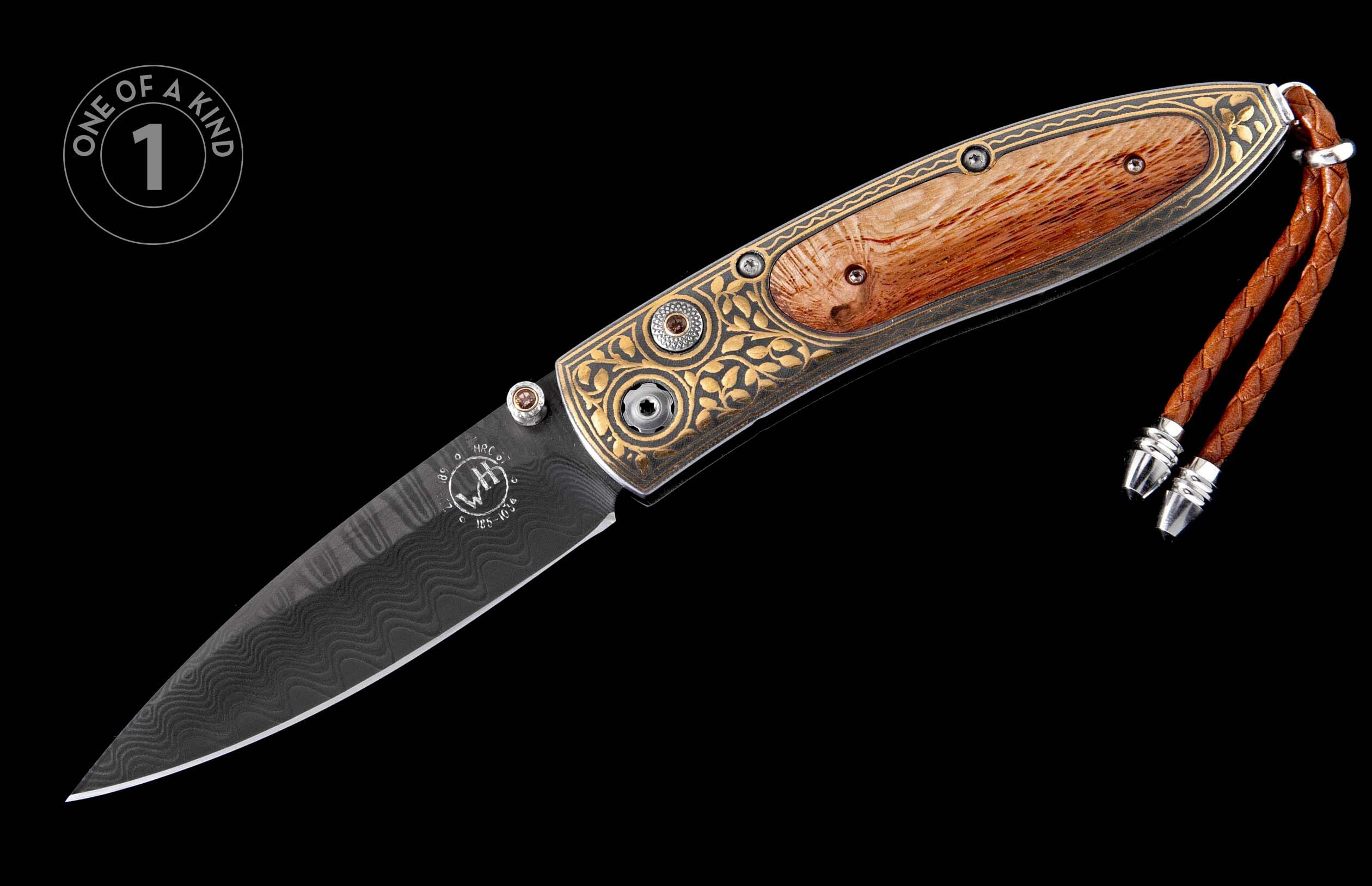 Ornate folding knife with dark damascus blade, gold engraved details, burl wood handle, and leather lanyard.