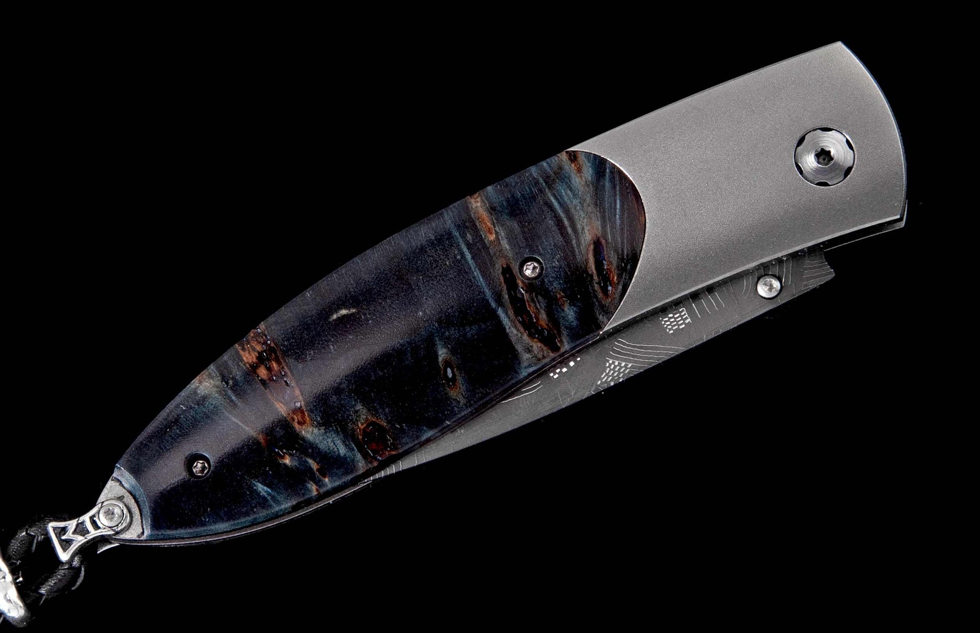 Folding knife with a dark blue and brown burl-patterned handle, satin titanium frame, and decorative etched details on the blade.