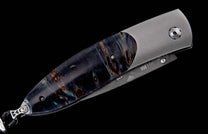 Folding knife with a dark blue and brown burl-patterned handle, satin titanium frame, and decorative etched details on the blade.