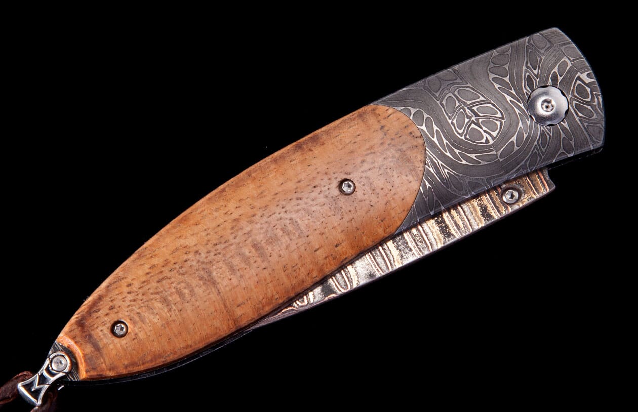 Light brown wooden folding knife from IKAIKA by Hildgund Exclusive, with intricate patterned Damascus steel bolster and spine.