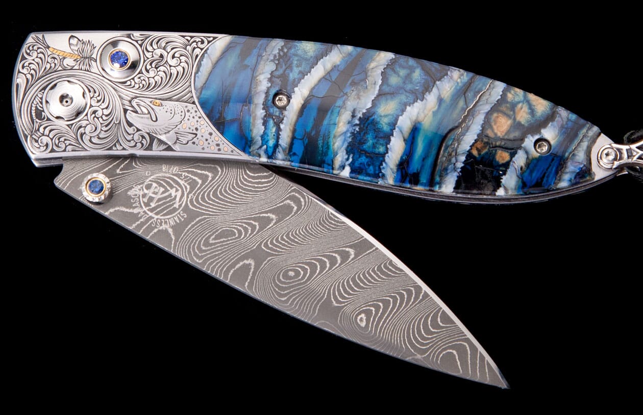 Ornate folding knife with Damascus steel blade, engraved silver handle featuring a fish and fly, blue/white patterned scale, and sapphire accents.