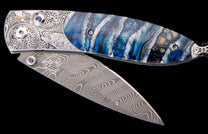 Ornate folding knife with Damascus steel blade, engraved silver handle featuring a fish and fly, blue/white patterned scale, and sapphire accents.
