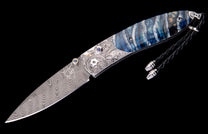 Artistic folding knife with a swirling Damascus blade, intricate silver engraving, and a striking blue, white, and brown layered handle.