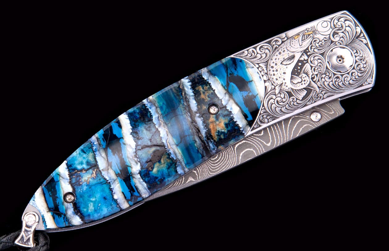 Custom folding knife with a blue, white, black, and brown patterned handle, silver bolster with fish engraving, and Damascus blade.