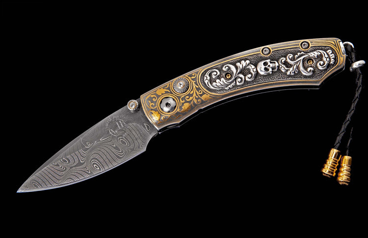 Damascus steel folding knife with an ornate silver and gold handle, skull motifs, crystal accents, and a black leather lanyard.