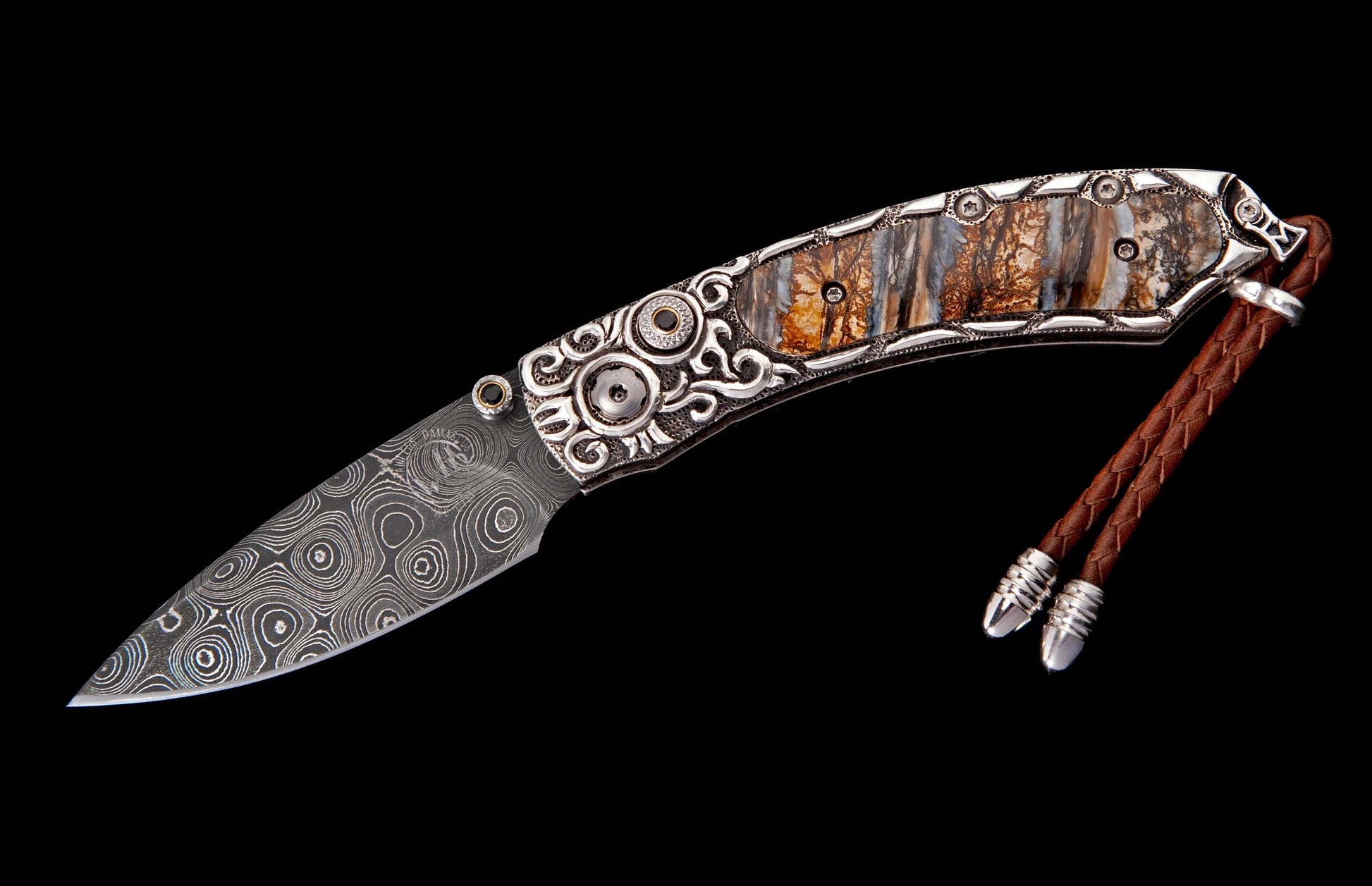 Folding knife with Damascus blade and ornate silver handle featuring petrified wood and black gem inlays, with a brown leather lanyard.