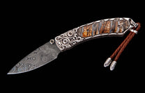 Folding knife with Damascus blade and ornate silver handle featuring petrified wood and black gem inlays, with a brown leather lanyard.