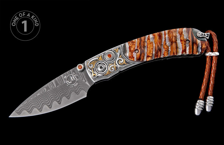 Side view of a folding knife with a wavy Damascus blade, ornate silver and gold scrollwork, orange gemstones, and a striped brown and white handle with a brown leather lanyard.