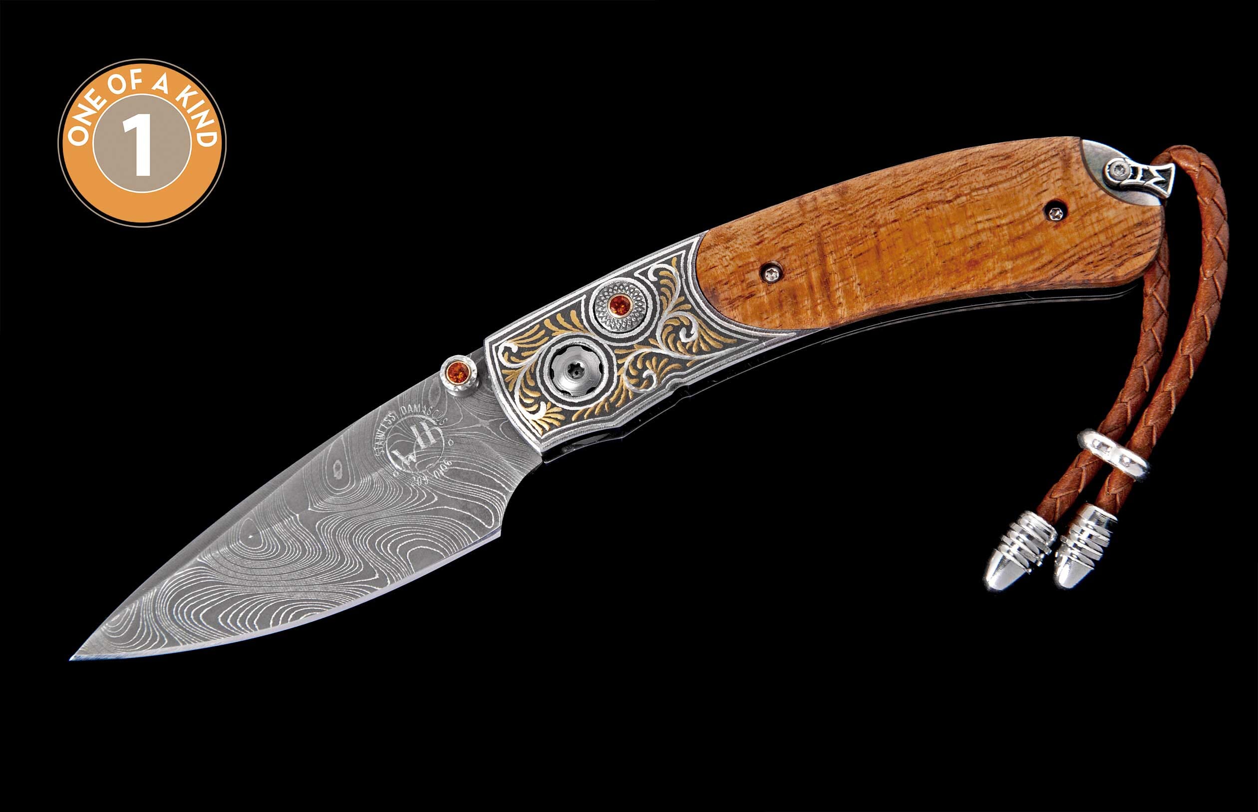 Ornate folding knife with a Damascus steel blade, wood handle, engraved bolsters featuring gemstones, and a braided leather lanyard.