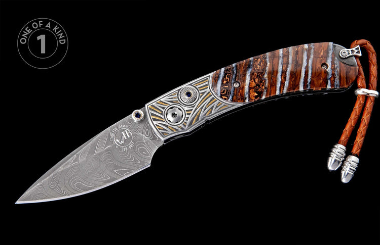 Damascus steel folding knife with a wavy patterned blade, ornate silver and gold handle with blue gems, brown striped scales, and a braided leather lanyard.