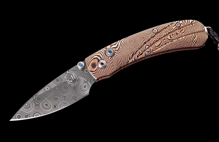 Damascus folding knife with a concentric circle patterned blade, brown wavy handle, blue gem accents, and a black braided lanyard.