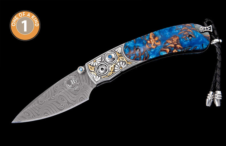 Damascus steel knife with engraved silver and gold bolster, blue gems, blue resin handle with natural inclusions, and braided lanyard.