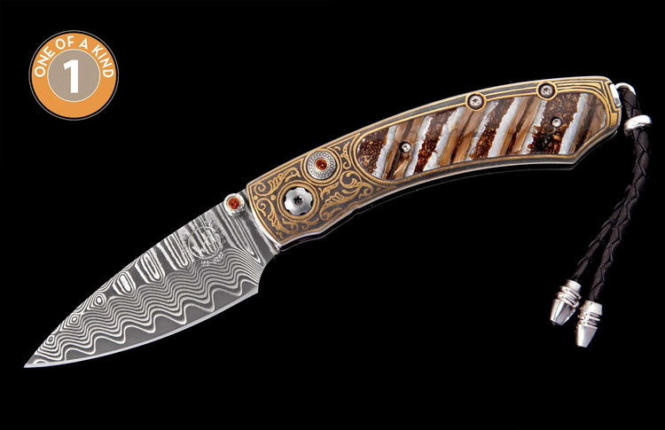 Ornate folding knife with wavy damascus blade, gold and silver engraved handle, segmented brown and white scales, orange gem thumb studs, and a black braided leather lanyard.