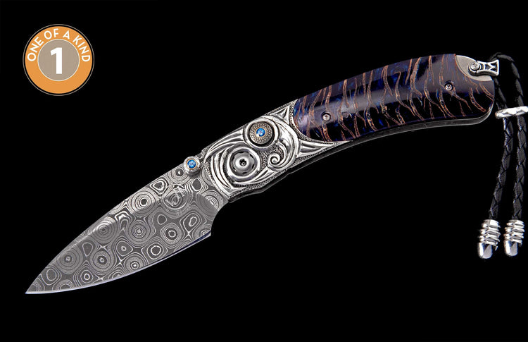 Knife with a swirled Damascus steel blade, ornate silver-colored handle accents with blue gemstones, and blue-gold patterned scales, with a black leather lanyard.
