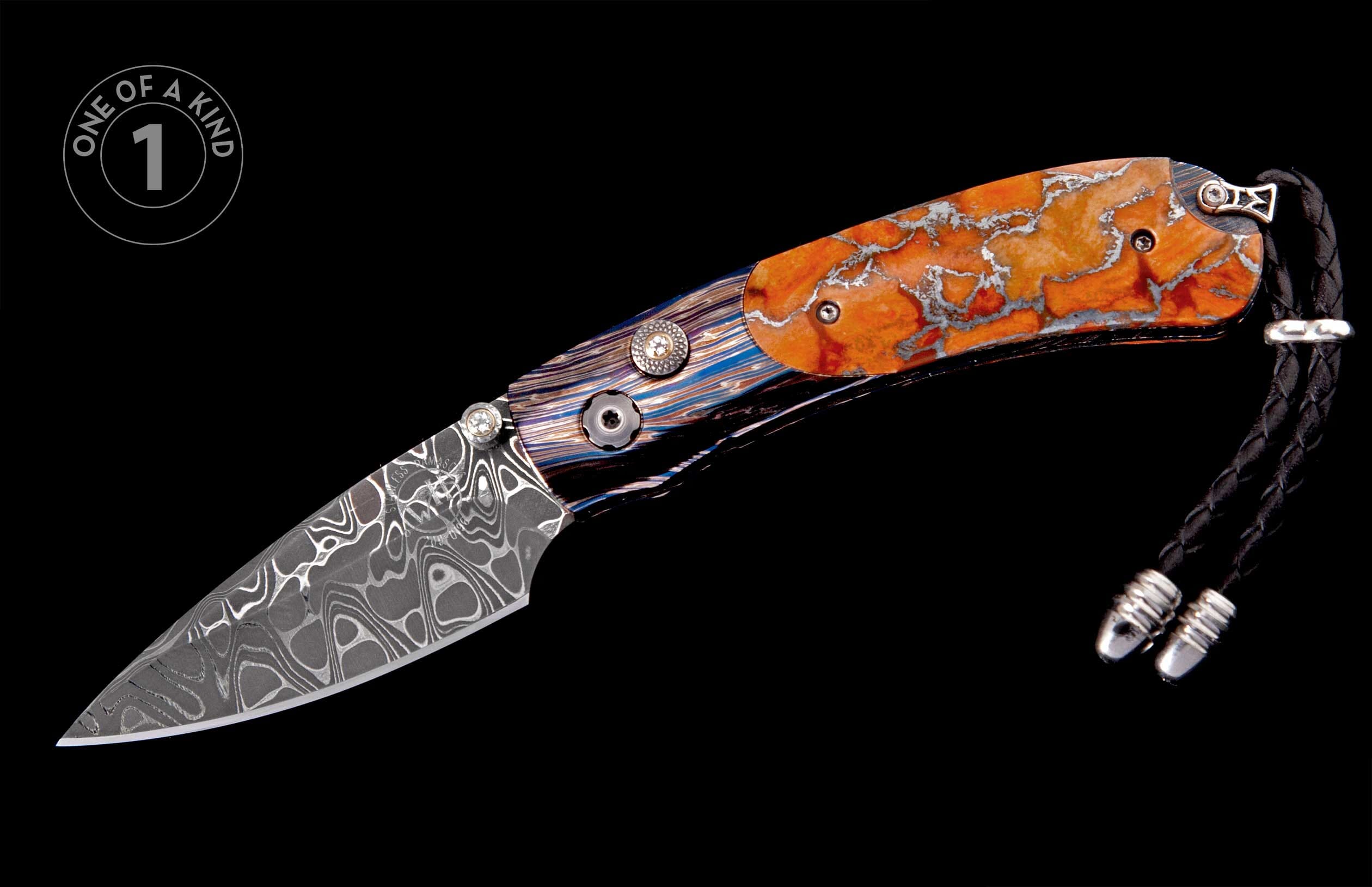 Folding knife with a Damascus blade, handle featuring striped and orange marbled scales with decorative studs, a black braided leather lanyard, and a "one of a kind" emblem.