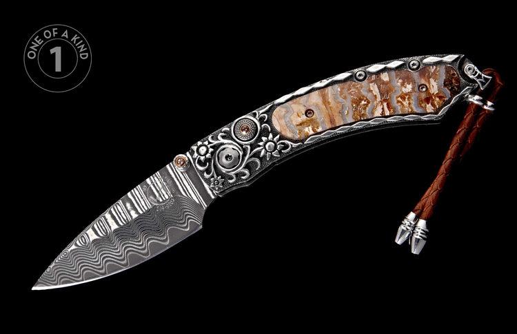 Ornate folding knife with a Damascus steel blade, petrified wood handle, intricate silver scrollwork, and a brown braided leather lanyard.