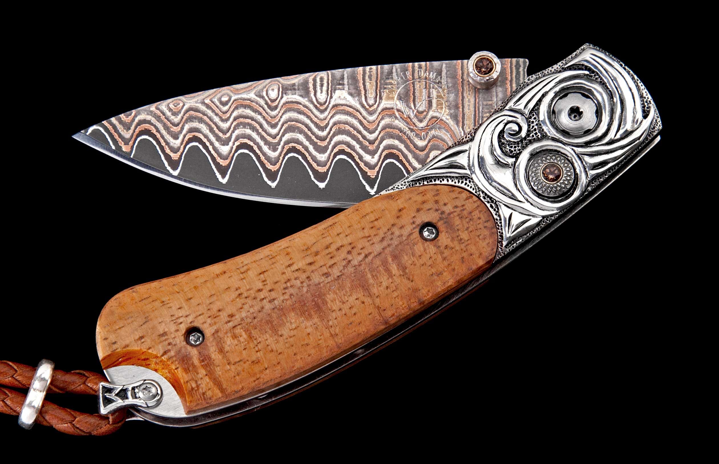 Ornate folding knife with wavy copper Damascus blade, light brown wooden handle, decorative silver metal bolster with brown gems, and braided leather lanyard.