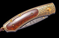 Ornate folding knife with dark wood handle, intricate gold scrollwork, and a patterned Damascus steel blade.