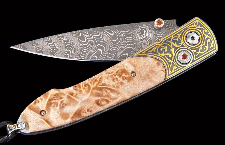 Folding knife with wavy Damascus blade, ornate gold and silver bolster with orange gems, and a burled wood handle.
