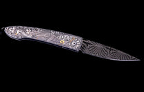 Ornate folding knife with an engraved handle featuring a mythological creature and gold accents, complemented by a distinctive damascus blade.