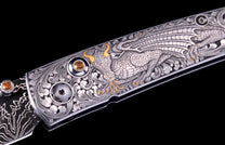 Silver knife with an intricately engraved dragon on the handle, accented with gold, orange gems, and a textured Damascus blade.