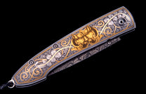 Custom knife with intricate silver floral and golden beast engraving on the handle, showing Damascus steel blade.