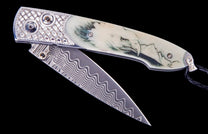 Partially open knife with a Damascus blade, light handle etched with an eagle and mountains, and a silver basketweave frame.