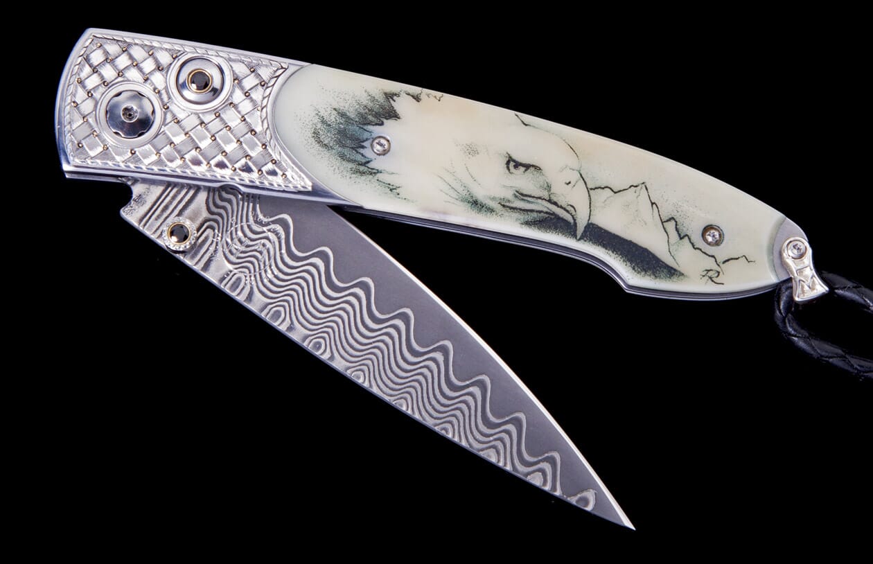 Partially open knife with a Damascus blade, light handle etched with an eagle and mountains, and a silver basketweave frame.