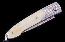 Custom knife with an ivory-colored handle, decorative silver bolster featuring a gold-dotted basketweave pattern, and a wavy etched spine.