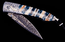 Ornate folding knife with patterned Damascus blade, engraved silver salamander bolster, blue gemstones, and a striped blue, white, and orange handle.