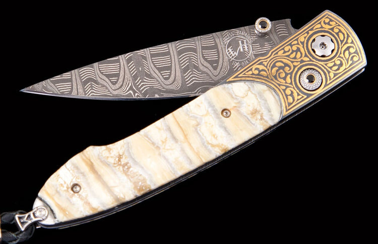 Folding knife with a patterned Damascus steel blade, intricate gold-engraved bolster, and a pale, naturally striated handle.