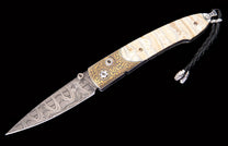 Ornate folding knife with Damascus blade, gold-toned scrollwork, light handle scales, and a black braided lanyard.