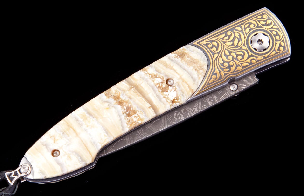 Fleur knife with cream and brown veined stone handle, gold swirling pattern, and damascus blade, shown angled.
