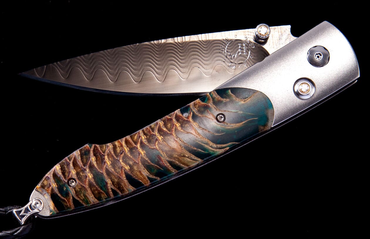 Partially open folding knife with a wavy patterned blade and a textured, scale-like handle in teal, gold, and brown.