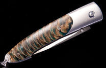 Knife with an ornate green and gold scaly handle and brushed silver-tone bolsters, shown at an angle.