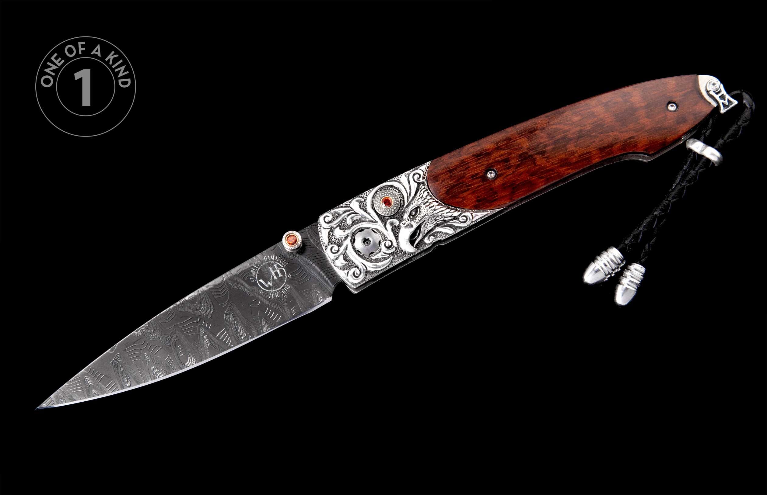 Ornate folding knife with Damascus steel blade, engraved silver bolster, red gems, and dark wood handle with braided leather lanyard.