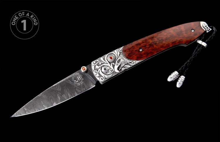 Ornate folding knife with Damascus steel blade, engraved silver bolster, red gems, and dark wood handle with braided leather lanyard.