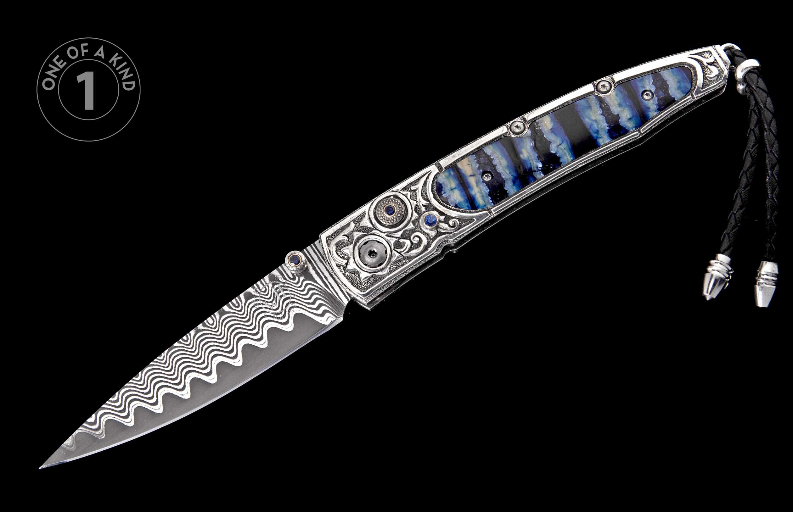 Ornate open folding knife featuring wavy Damascus steel blade, silver handle with blue striped inlay, and sapphire accents.