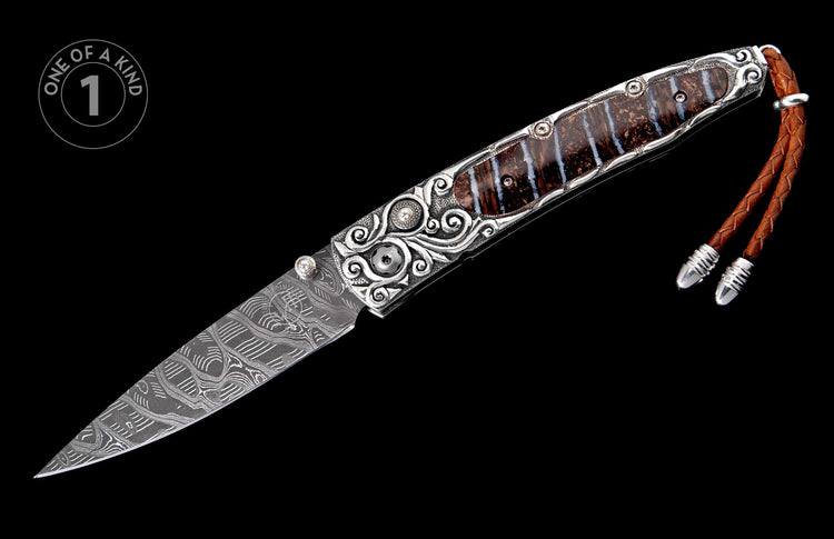 Damascus steel folding knife with ornate silver handle featuring fossilized wood inlay and a braided leather lanyard.