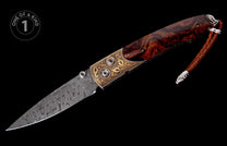 Folding knife with a damascus steel blade, decorative gold-colored scrollwork, dark gemstone, rich reddish-brown wood handle, and a braided leather lanyard.