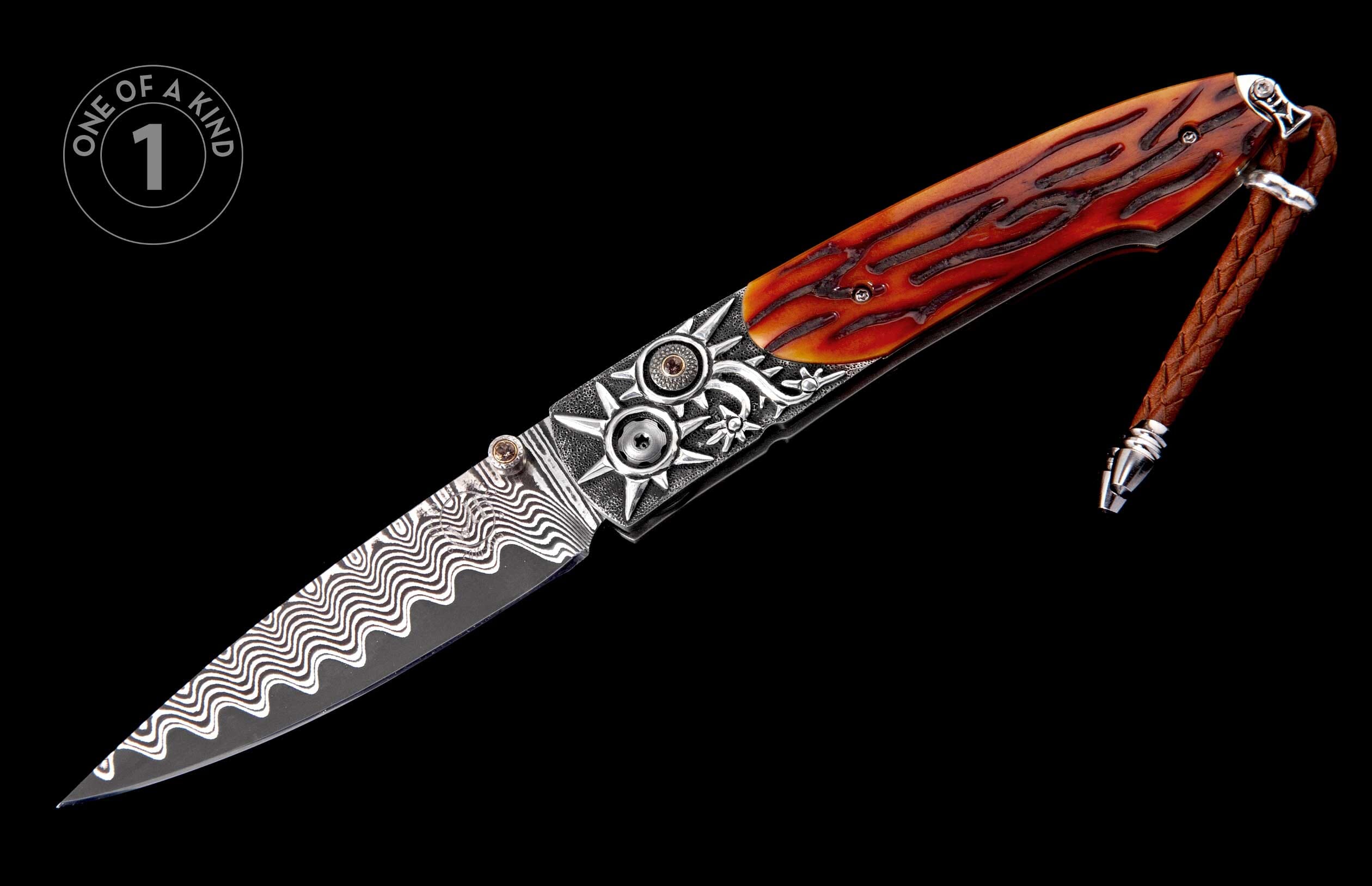 Ornate folding knife with a wavy Damascus steel blade and an orange antler-textured handle, decorated with silver sun motifs, brown gems, and a braided leather lanyard.