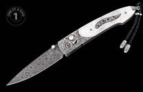 Folding knife with a white textured handle, intricate silver engraving, blue opal inlays, a patterned Damascus blade, and a black braided lanyard.