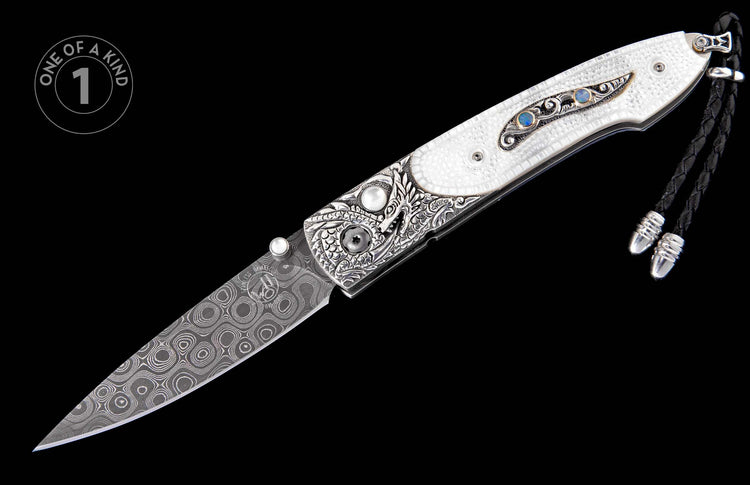 Folding knife with a white textured handle, intricate silver engraving, blue opal inlays, a patterned Damascus blade, and a black braided lanyard.