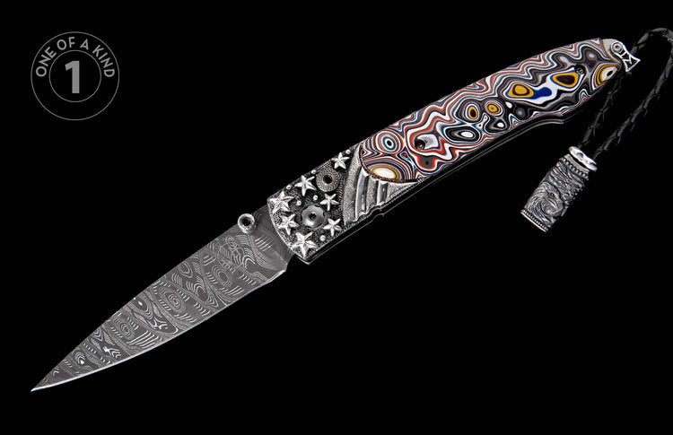 Open folding knife with Damascus blade, vibrant multi-color wavy patterned handle, and detailed silver-toned metal bolster with stars and eagle lanyard.