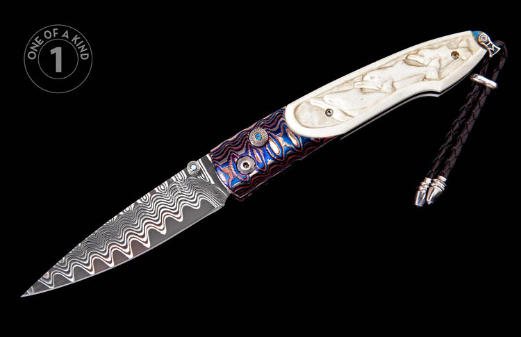 Custom knife with wavy Damascus blade, carved bone handle featuring marine life, blue gemstone, and braided black leather lanyard.