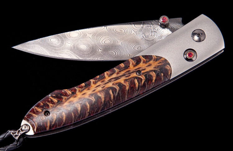 A folding knife with a patterned Damascus steel blade, a textured dark brown and tan handle, and red jewel accents.