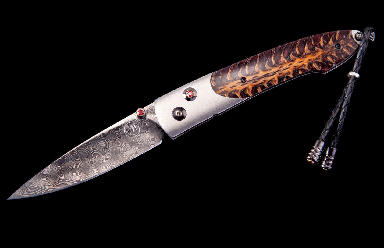Folding knife with a patterned Damascus blade, distinctive brown wood handle with red accents, and a black leather lanyard.
