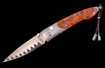 Oceana folding knife with orange and silver patterned handle, wavy Damascus blade, and braided leather lanyard.